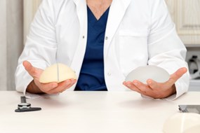 arts-met-siliconen-implantaat-voor-borstvergroting-ruimte-voor-tekst-plastisch-chirurg-handen-met-siliconen-borstimplantaten-cosmetische-chirurgie_99272-1449